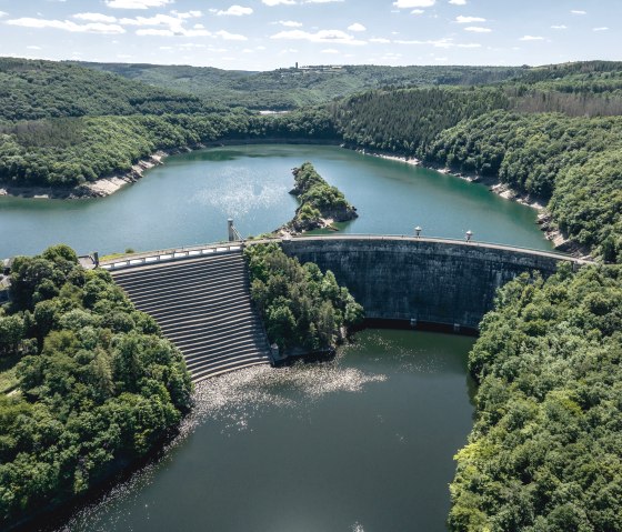 Aerial view of the Urft dam with the Urft dam wall, surrounded by densely wooded hills and blue water under a clear sky., © Eifel Tourismus GmbH, Dennis Stratmann - finanziert durch REACT-EU Aerial view of the Urft dam with the Urft dam wall, surrounded by densely wooded hills and blue water under a clear sky., © Eifel Tourismus GmbH, Dennis Stratmann - finanziert durch REACT-EU