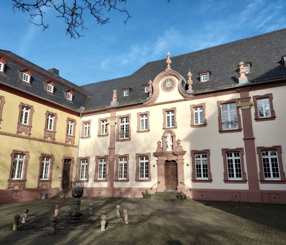 Barocke Fassade des Klosters Steinfeld mit Uhr und Statue im Innenhof, umgeben von blauem Himmel und Bäumen., © Sweco GmbH Barocke Fassade des Klosters Steinfeld mit Uhr und Statue im Innenhof, umgeben von blauem Himmel und Bäumen., © Sweco GmbH