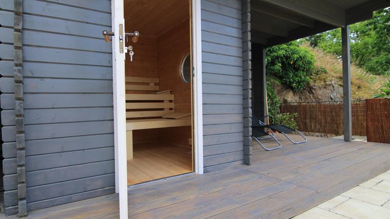 Eine moderne Sauna mit Holzverkleidung und einem einladenden Eingang. Der Außenbereich ist mit Steinen und einer Holzverkleidung gestaltet.