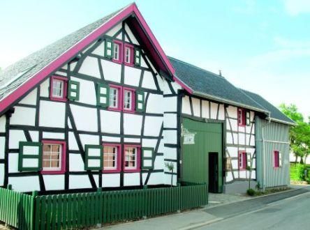 Ein traditionelles Fachwerkhaus mit weißem Putz und schwarzen Balken. Die Fenster sind grün und pink, was dem Gebäude einen lebhaften Charme verleiht.