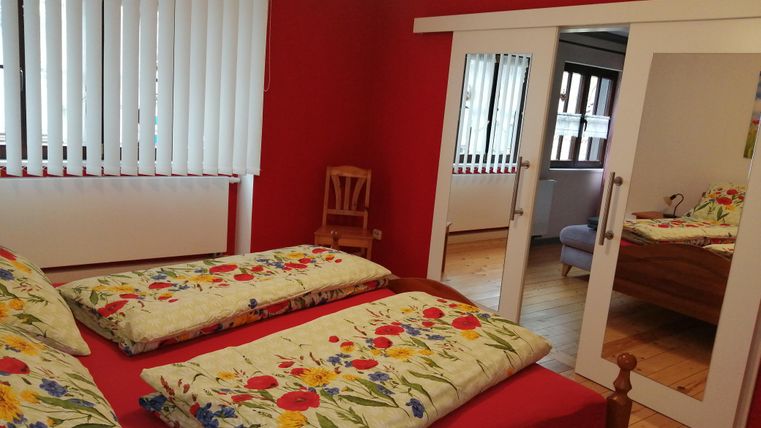 Ein gemütliches Schlafzimmer mit roter Wandfarbe. Es gibt zwei Betten mit blumigen Bettdecken und einen Spiegel.