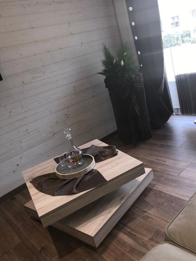 Ein stilvoller Wohnraum mit einem modernen Tisch aus Holz und einem dekorativen Arrangement. Im Hintergrund sind Pflanzen und elegante Vorhänge sichtbar.