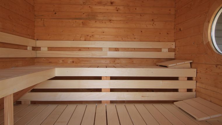Ein heller Saunaraum aus Holz mit zwei Bänken und runden Fenstern. Die Atmosphäre ist ruhig und entspannend.