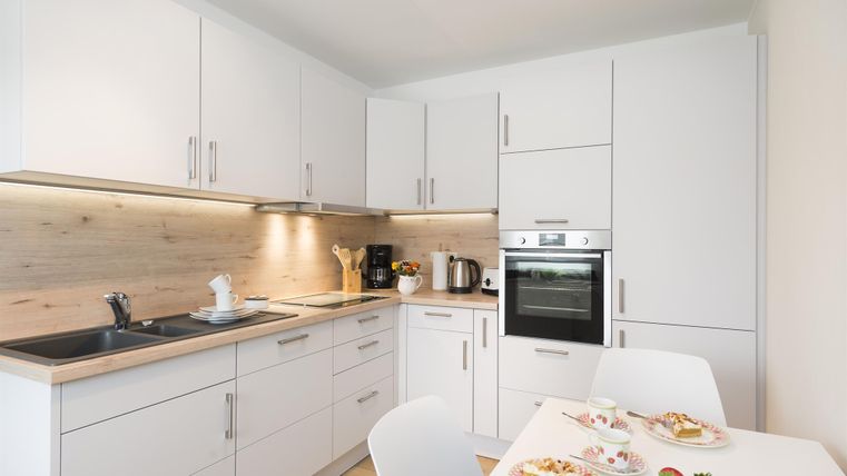 Eine moderne Küche mit weißen Schränken und einer Holzarbeitsplatte. Auf dem Tisch liegen Teller mit Kuchen und frischen Erdbeeren.