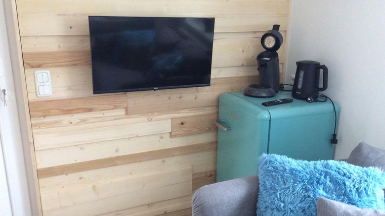 Ein moderner Wohnraum mit einer holzverkleideten Wand. Ein Fernseher, ein Kühlschrank in Blau und eine Kaffeemaschine sind gut sichtbar.