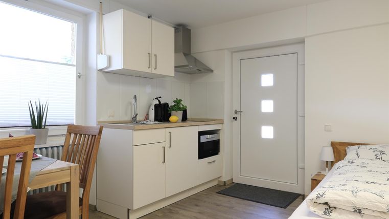 Eine helle, moderne Küche mit einem Essbereich und einem Schlafbereich. Die Einrichtung ist funktional und minimalistisch.