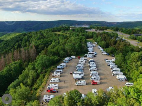 Ein großer Campingplatz auf einem Hügel, umgeben von Bäumen und Bergen. Zahlreiche Wohnmobile sind auf gravelboden geparkt.