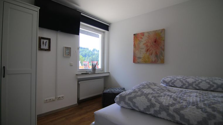 Ein helles Schlafzimmer mit einem großen Fenster und einem bunten Gemälde an der Wand. Das Bett ist mit einem gestreiften Bettbezug und Kissen dekoriert.