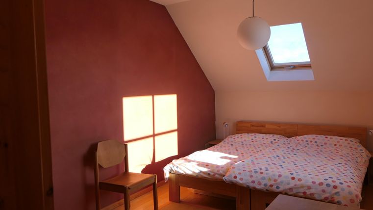 Ein gemütliches Schlafzimmer mit einem Doppelbett und einer Holzkommode. Durch das Fenster fällt sanftes Licht auf den Boden.