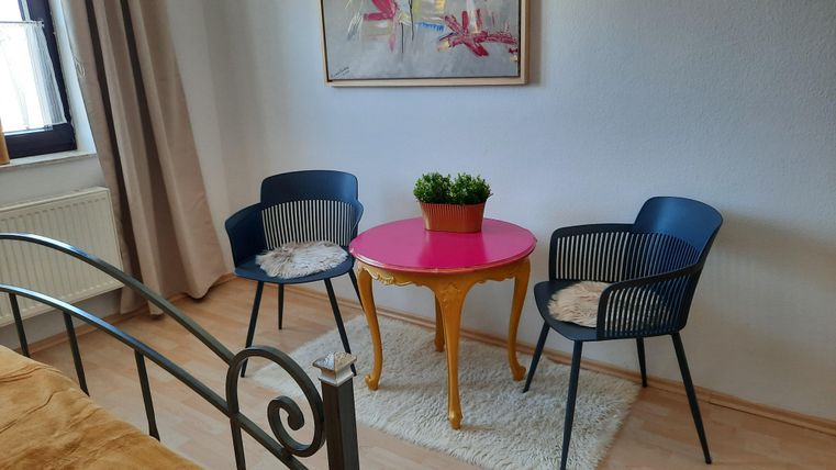 Ein gemütlicher Raum mit zwei Stühlen und einem runden Tisch in der Mitte. Auf dem Tisch steht eine Pflanze in einem Topf.