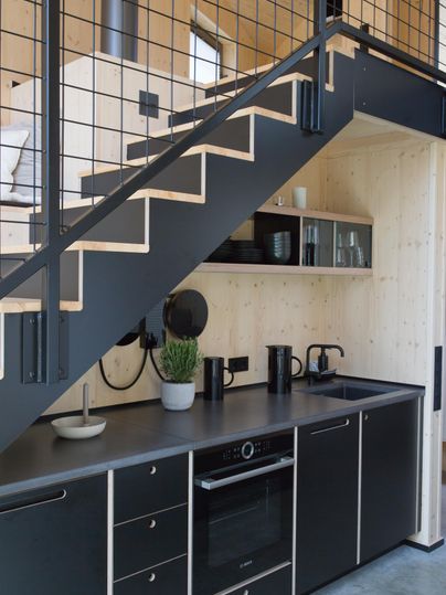 Eine moderne Küche unter einer Treppe mit schwarzen Schränken und einer einfachen, eleganten Einrichtung. Der Raum wirkt hell und einladend.