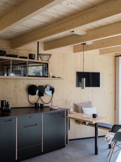 Eine moderne Küche mit Holzregalen und klaren Linien. Der Raum ist hell und freundlich, mit einem Tisch und Stühlen für geselliges Beisammensein.