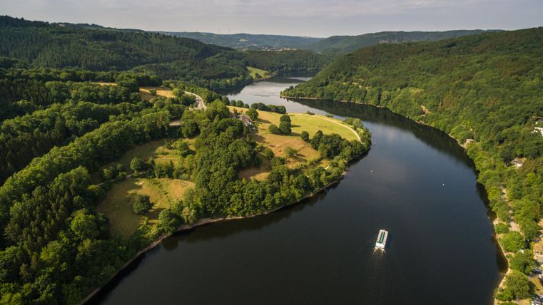 Eine malerische Flusslandschaft mit sanften Hügeln und üppigem Grün. Ein Boot fährt ruhig auf dem Wasser.