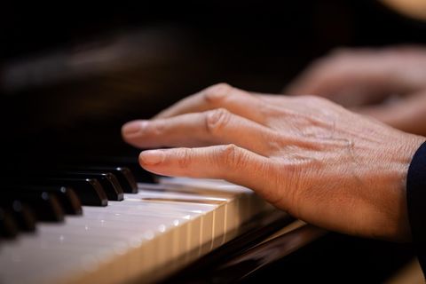 Eine Hand spielt Klavier. Die Tasten sind gut sichtbar, während die Finger in Bewegung sind.