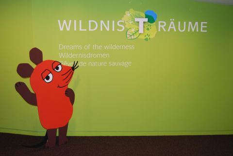 Das Bild zeigt die Maus von Die Sendung mit der Maus vor dem Wildnis-Träume Schriftzug.