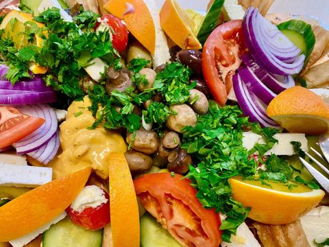 Ein bunter Salat mit frischem Gemüse, darunter Tomaten, Gurken, und Paprika, garniert mit frischem Koriander. Die Präsentation umfasst auch einige Käse- und Brotstücke.