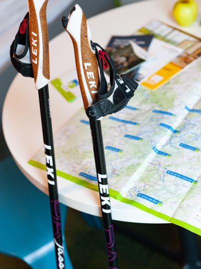 Zwei Wanderstöcke stehen auf einem Tisch neben einer Landkarte. Ein gelbes Objekt ist ebenfalls sichtbar.