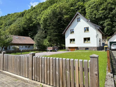 Ein hübsches Haus umgeben von Bäumen und Wiese. Im Vordergrund steht ein Holzzaun, der das Grundstück abgrenzt.