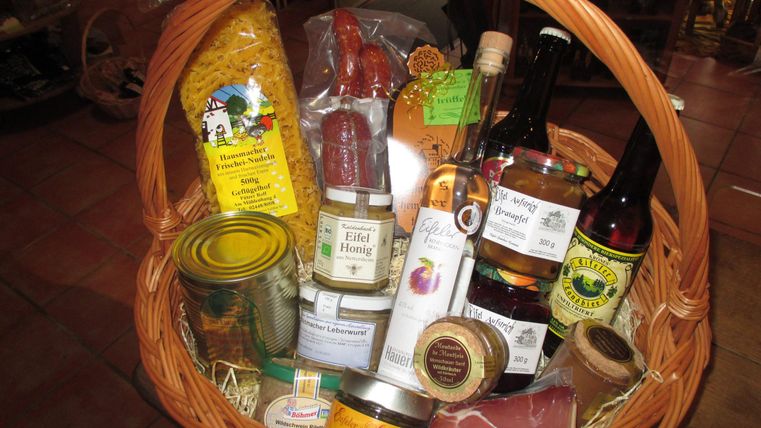 Ein Korb voller regionaler Lebensmittel, darunter Nudeln, Honig, Marmelade und Getränke. Die Produkte sind sorgfältig arrangiert und vermitteln ein rustikales, einladendes Ambiente.