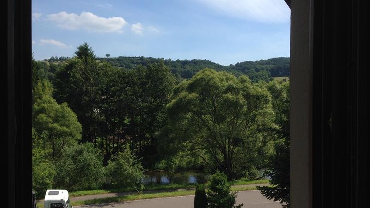 Ausblick auf eine grüne Landschaft mit vielen Bäumen und einem ruhigen Fluss. Der Himmel ist klar und blau.