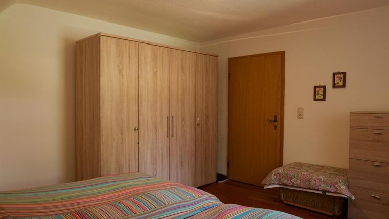 Ein einfaches Schlafzimmer mit bunten Bettwäsche in Streifen. Es gibt einen Holzschrank, eine Kommode und eine Tür, die zum Flur führt.