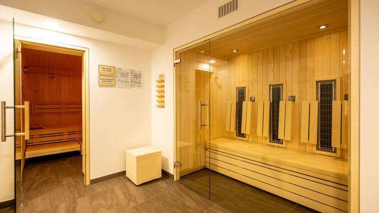 Ein modernes Saunabereich mit Holzverkleidung und großen Fenstern. Die rechte Seite zeigt eine Infrarot-Sauna und auf der linken Seite befindet sich eine traditionelle finnische Sauna.