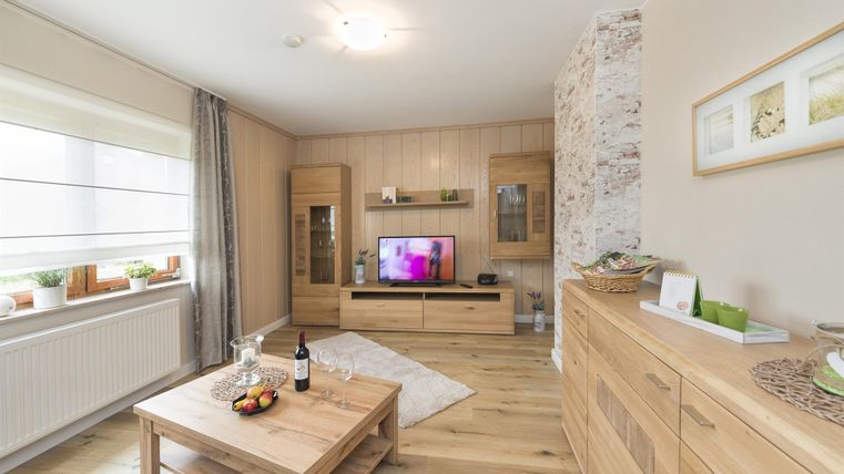 Ein modernes Wohnzimmer mit hellem Holz und eleganten Möbeln. Der Raum verfügt über einen Fernseher und eine gemütliche Atmosphäre.