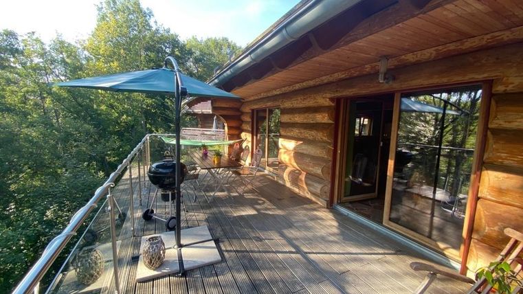 Eine Holzterrasse mit Blick ins Grüne und einem Sonnenschirm. Ein Grill und bequeme Stühle laden zum Entspannen ein.