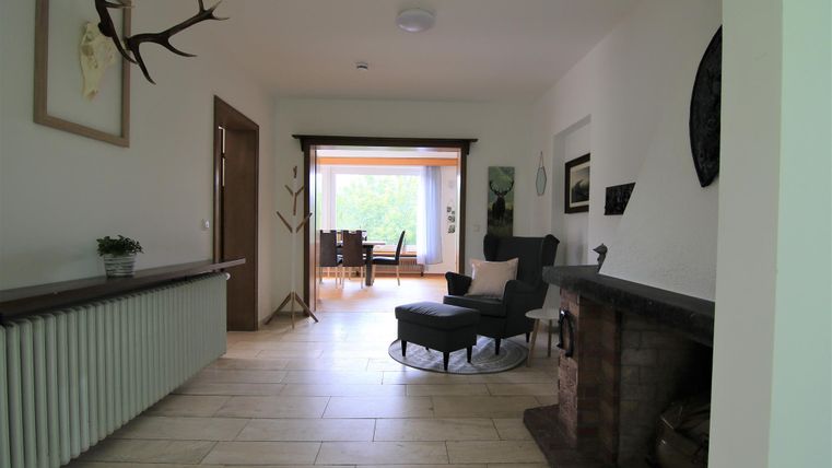 Ein heller und geräumiger Flur mit einem gemütlichen Sessel und einem Blick auf den Essbereich. An der Wand hängen einige dekorative Elemente, die dem Raum Charakter verleihen.