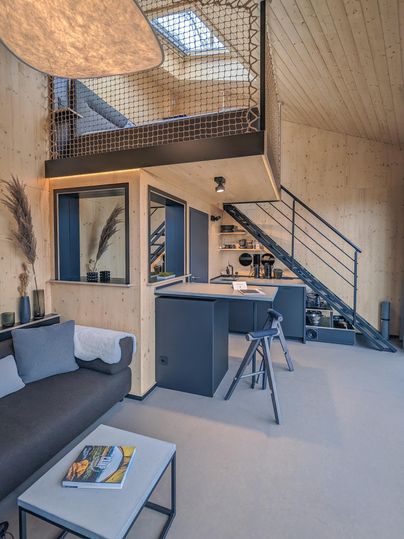 Ein modernes, helles Wohnzimmer mit Holzakzenten und einer offenen Treppe. Die Wohnung hat eine gemütliche Atmosphäre und eine offene Küchenzeile.