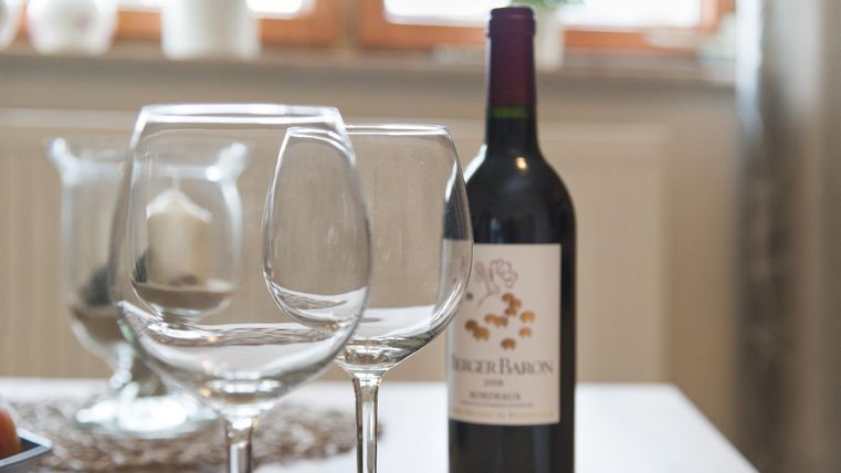 Ein eleganter Tisch mit zwei Weingläsern und einer Flasche Rotwein. Im Hintergrund sind Pflanzen und Fenster sichtbar.