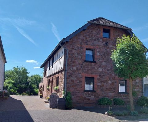 Ein traditionelles, rotsteingedecktes Haus mit einem klaren blauen Himmel im Hintergrund. Der Garten hat einige grüne Pflanzen und Bäume.