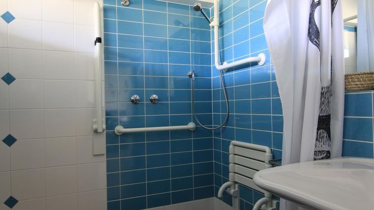 Ein Badezimmer mit blauen Fliesen und einer Dusche. Es gibt einen Heizkörper und eine rechteckige Waschbeckenablage.