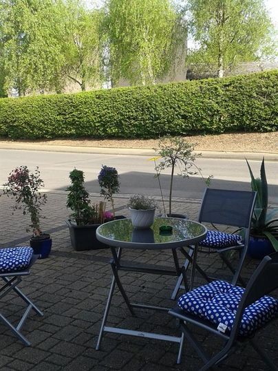 Ein gemütlicher Außenbereich mit einem Tisch und Stühlen. Umgeben von Pflanzen und grüner Bepflanzung.