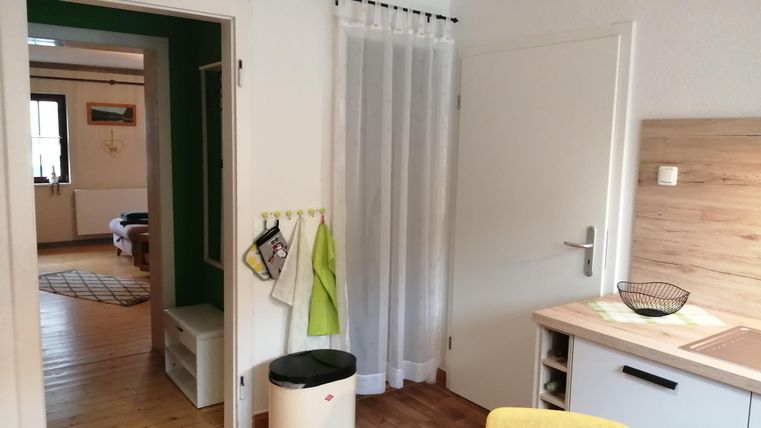 Ein helles Zimmer mit Holzfußboden und moderner Kücheneinrichtung. Die Tür führt zu einem weiteren Raum mit einem gemütlichen Ambiente.