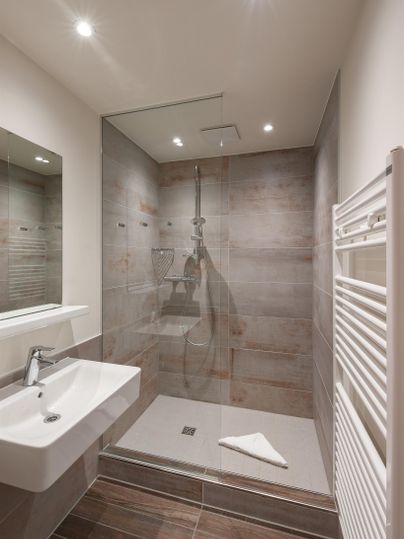 Ein modernes Badezimmer mit einer ebenerdigen Dusche und hellen Wänden. Das Waschbecken ist elegant und die Beleuchtung sorgt für eine angenehme Atmosphäre.