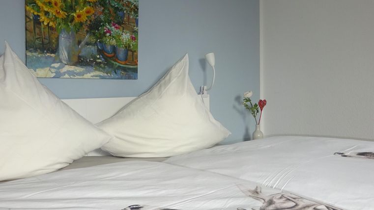 Ein gemütliches Schlafzimmer mit einem weißen Bett und zwei Kopfkissen. An der Wand hängt ein Gemälde mit Sonnenblumen.