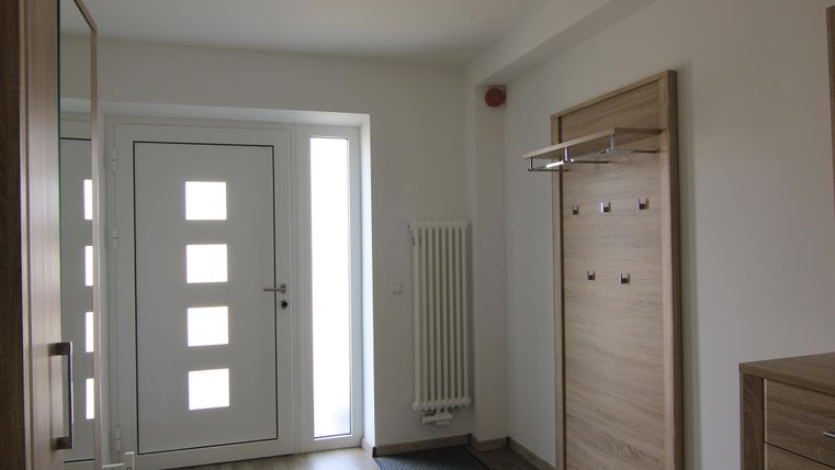 Ein heller Flur mit einer modernen Eingangstür und einem Garderobenschrank. Der Boden ist aus Holz und ein Teppich liegt vor der Tür.