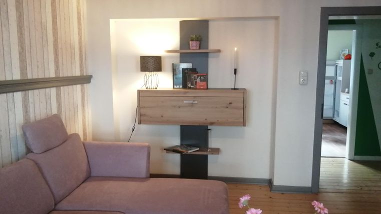 Ein gemütliches Wohnzimmer mit einem bequemen, lila Sofa und dekorativen Regalen an der Wand. Es gibt eine kleine Pflanze und eine Kerze auf dem Regal.