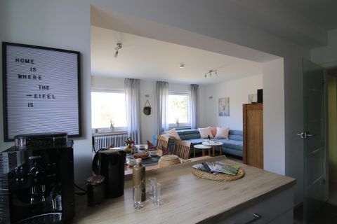 Ein helles und modernes Wohnzimmer mit gemütlichen Sofas und einem Tisch. Die Fenster sorgen für viel Tageslicht und eine einladende Atmosphäre.
