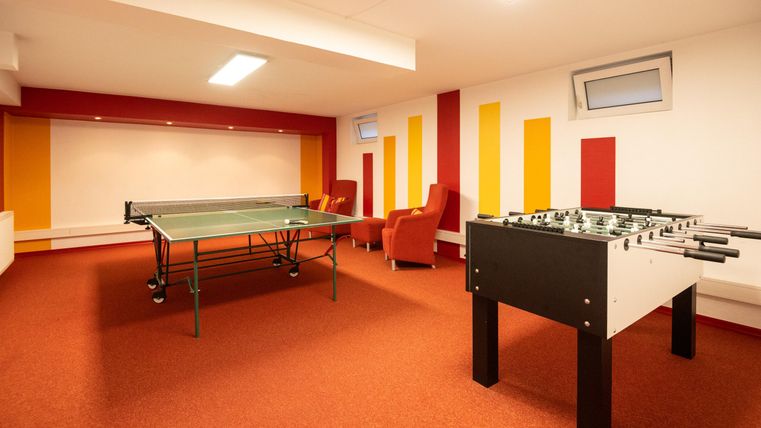 Ein gemütlicher Freizeitraum mit einem Tischtennistisch und einem Kicker. Die Wände sind in warmen Farben gestaltet, und es gibt bequeme Stühle.