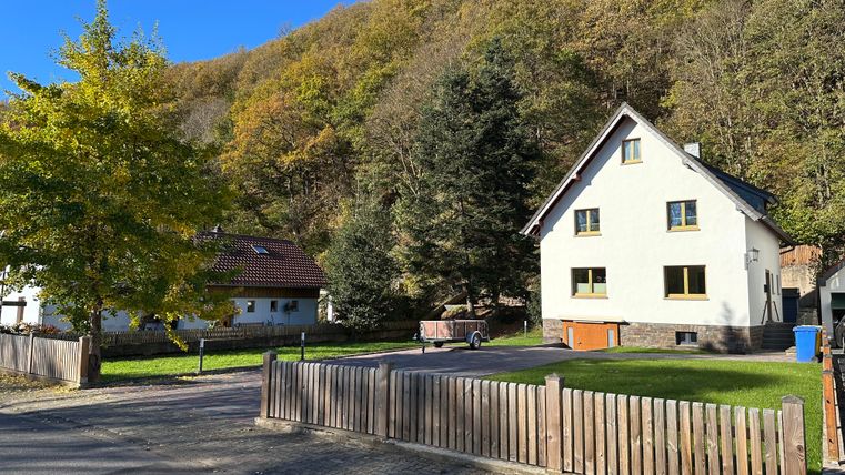 Ein ruhiges Wohngebiet mit einem modernen Haus und einer grünen Wiese. Im Hintergrund sind Bäume und Hügel zu sehen, die einen herbstlichen Eindruck vermitteln.