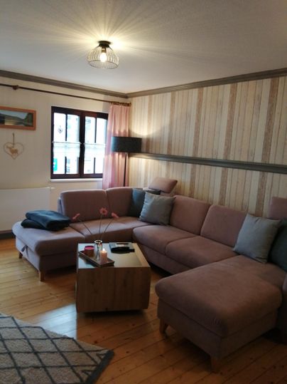 Ein gemütliches Wohnzimmer mit einem pinken Sofa und einem kleinen Couchtisch. Die Wände sind mit Holzvertäfelungen und einer hellen Tapete dekoriert.