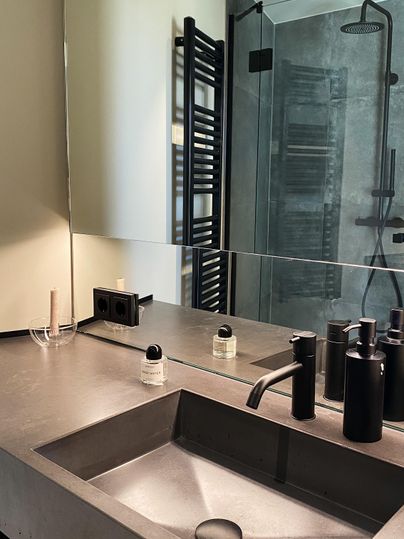 Ein modernes Badezimmer mit einem schlichten Waschbecken und stilvollen, schwarzen Accessoires. Im Hintergrund ist eine Dusche und ein Handtuchwärmer sichtbar.