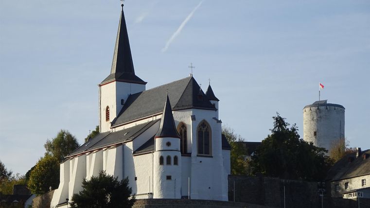 Eine beeindruckende Kirche mit einem hohen Turm und einem weißen Kleid. Im Hintergrund sieht man einen alten Turm auf einem Hügel.