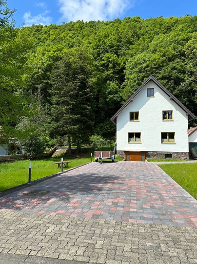 Ein modernes Haus umgeben von Bäumen auf einer schönen Wiese. Der gepflasterte Weg führt zur Haustür.