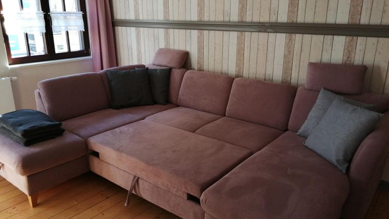 Ein modernes, helles Wohnzimmer mit einem großen, beigen Ecksofa. Das Sofa hat Kissen und ist vor einer Holzvertäfelung platziert.