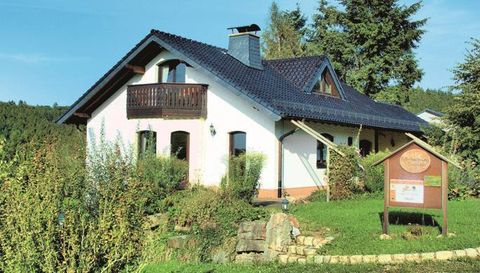 Ein charmantes Haus mit einem dunkelblauen Dach und einem kleinen Balkon. Es ist von grünen Pflanzen und Bäumen umgeben.