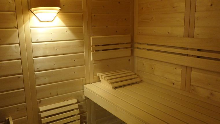 Eine Holzsauna mit Sitzbänken und sanfter Beleuchtung. Der Raum strahlt Gemütlichkeit und Entspannung aus.