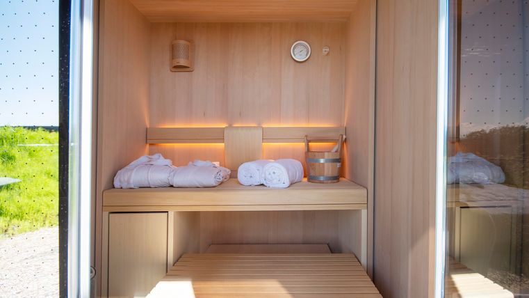 Eine moderne Sauna aus Holz mit Handtüchern und einem kleinen Eimer. Sanftes Licht und eine entspannende Atmosphäre laden zum Entspannen ein.